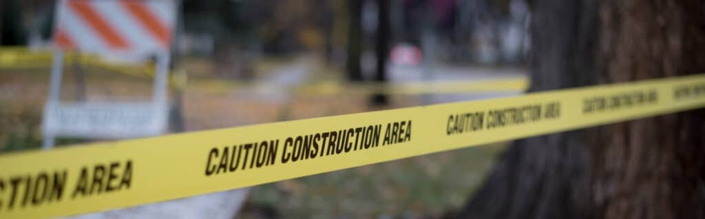 Yellow caution tape marked "construction area" strung across a construction site near trees, indicating restricted work zone
