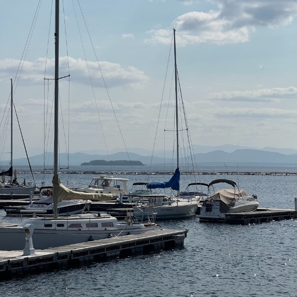 Sailboats moored at a dock on Lake Champlain with forested mountains visible in the distance